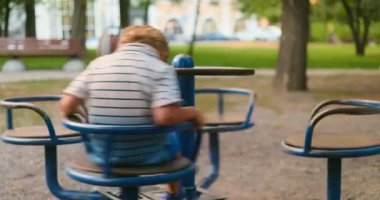 Neşeli genç çocuk güneşli bir günde parkın bahçesinde mavi bir atlıkarıncada dönüyor.