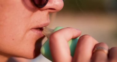 Renkli bir tüp kullanan bir kadının makro çekimi, sıcak doğal ışıkta buhar üflemesi, yaşam tarzını ve alışkanlıklarını ön plana çıkarması. Yüksek kalite 4k görüntü