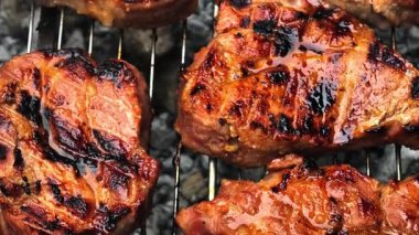 Izgara ızgarada ızgara et cızırtısının yakın çekim videosu. Et, lezzetli bir açık hava pişirme deneyimini vurguluyor..