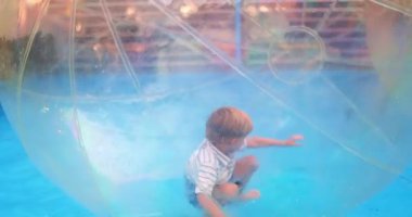 Bir çocuk havuzda yüzen şişme bir su topunun içinde oynamaktan hoşlanır. Şeffaf küre, su yüzeyinde eğlenceli ve güvenli bir hareket sağlıyor ve keyifli bir deneyim yaratıyor..