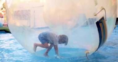 Bir çocuk şeffaf şişme bir su topunun içinde oynamaktan, yüzmekten ve havuz yüzeyinde yürümekten hoşlanır. Etkinlik, güvenli ve kapalı bir ortamda eğlence ve heyecanı yakalıyor..