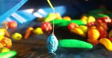 Renkli plastik balık ve çubuklarla dolu bir oyuncak balık avlama oyunu gösteren canlı bir video. Sahne eğlenceli etkileşimleri yakalıyor, aktivitenin doğasını vurguluyor..