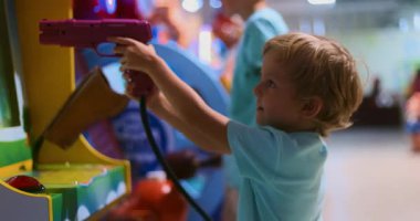Küçük bir çocuk oyun salonunda şevkle atış oyunu oynuyor. Renkli çevre ve parlak ışıklar eğlence için eğlenceli ve çekici bir atmosfer yaratır..