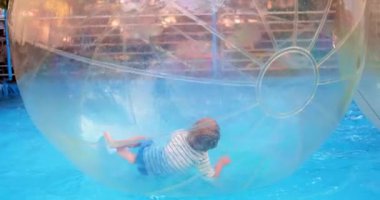 Bir çocuk, havuzun yüzeyinde yüzen ve yuvarlanan, şişme bir su topunun içinde oynamaktan hoşlanır. Şeffaf top güvenli ve eğlenceli su aktivitelerine olanak sağlıyor.