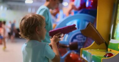 Küçük bir çocuk, kapalı bir eğlence merkezinde atari oyunu oynuyor. Renkli ortam ve oyuna odaklanma hareketli ve çekici bir atmosfer yaratıyor..