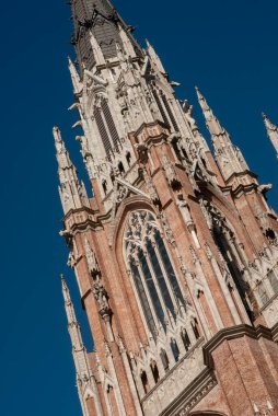 Bir katedral kulesinin süslü detayları parlak mavi bir gökyüzüne karşı duruyor. Karmaşık mimari ve işçiliğini gözler önüne seriyor.