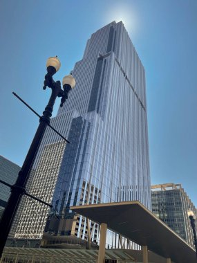 Modern glass skyscraper reaching towards a bright sun, with a street light and bus stop canopy in the foreground clipart