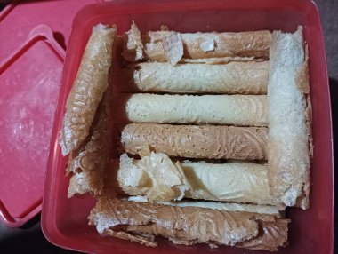 İçi gevrek yuvarlanmış waffle kurabiyeleriyle dolu kırmızı plastik bir kap.