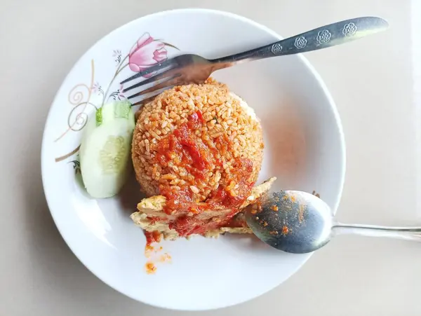 Baharatlı soslu kızarmış pirinç ve beyaz tabakta salatalık.