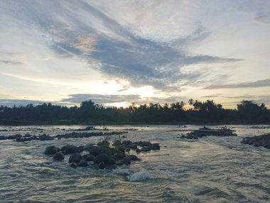 Doğanın sükunetini kayalık bir nehrin üzerinde güzel bir günbatımı görüntüsüyle yakala. Seyahat, doğa ve rahatlama projeleri için mükemmel..