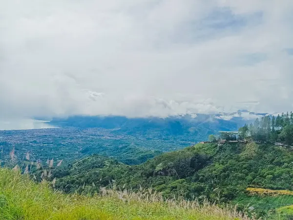 Bulutlu bir gökyüzünün altında dağlarla çevrili yemyeşil bir göl manzarası..