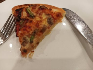 Beyaz tabakta çatal ve bıçakla dilimlenmiş tuzlu pizza.
