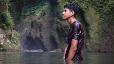 Kestane rengi gömlekli genç adam Şelalede Suda Duruyor