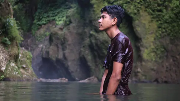 Kestane rengi gömlekli genç adam Şelalede Suda Duruyor