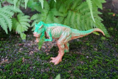 Oyuncak dinozor heykelciği gerçek doğa manzarasında.