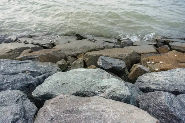 Close-up photo of blue rocks on the beach, calm ocean waves
