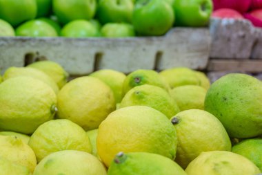 Piles of lemons are stacked in rows in a bustling wet market with a blurred apple background. fully ripe fruit clipart