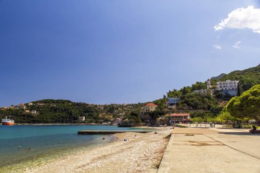 Sami, Kefalonia, Yunanistan sahillerine bakıyorum. Arka planda liman olan taştan bir kumsal. Mavi deniz ve gökyüzü ile sıcak güneşli bir gün. Yüksek kalite fotoğraf