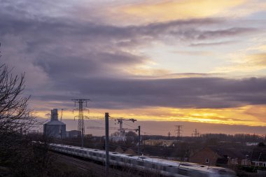 Endüstriyel bir arazide güneş batıyor. Bir elektrik santralinin üzerinde güzel bir gökyüzü, vinçler ve hızla geçen bir tren. Yüksek kalite fotoğraf