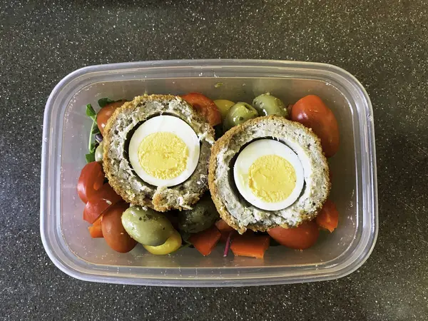 A tasty packed lunch of salad and scotch eggs in a plastic container. High quality photo