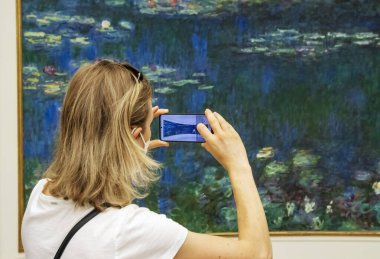 Paris, Fransa - 29 Temmuz 2022 Cuma: LOrangerie sanat galerisinde Monet 'in nilüferlerini cep telefonuyla fotoğraflayan kadın. Yüksek kalite fotoğraf