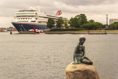 Copenhagen, Denmark - July 4th 2019: The little mermaid statue in Copenhagen harbour, with a cruise ship and a sea plane in the background. High quality photo clipart