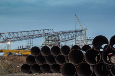 Konveyör galerisinin arka planındaki iskelenin inşaatı. Metal borular yerde duruyor..