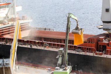 Loading of corn into the ship's hold at the same time by a mobile conveyor and a grab manipulator clipart