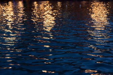 Glare of night city lights on the water ripple. City lights. Lantern light. Sea ripple.