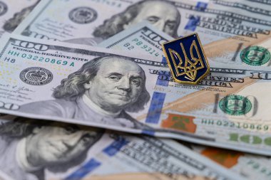 Yüz dolarlık banknotlar masaya saçıldı. Ukrayna arması şeklindeki rozet dolarların üzerinde yatıyor. Ukrayna 'nın ulusal amblemi bir mızraktır. Birleşik Devletler 'in Ukrayna' daki finansmanı.