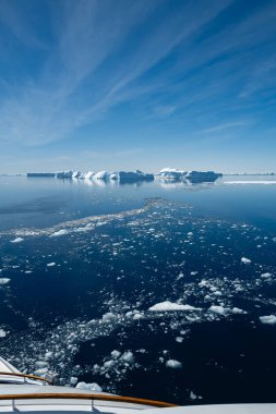 Vertical shot of the cruise ship approaching the group of blue icebergs clipart