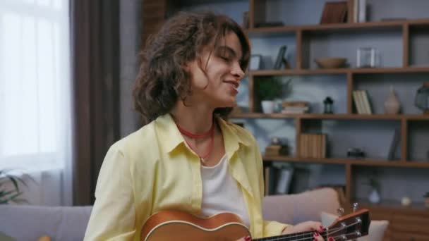 Beautiful Hipster Girl Yellow Shirt Plays Sings Ukulele Sofa Apartment — Stock video