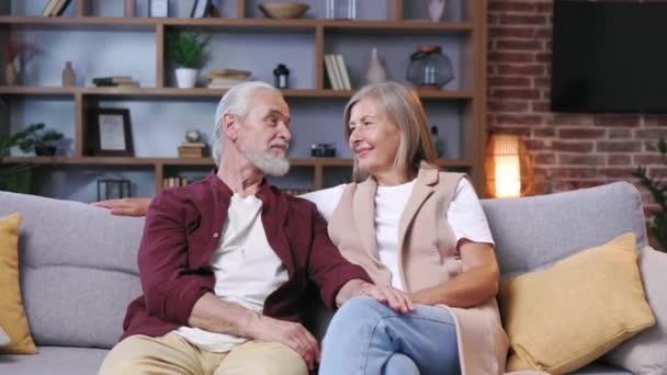 这对成熟快乐的夫妇低着头坐在沙发上 白头发的丈夫和妻子互相拥抱 快乐老年人的关系 中年祖父母一起在家里放松 — 图库视频影像