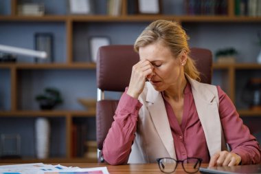 Tired businesswoman after exhausting paperwork taking off eyeglasses feeling nack pain. Head ache, bad vision, chronic fatigue and eyestrain concept. Burnout and overwork concept.