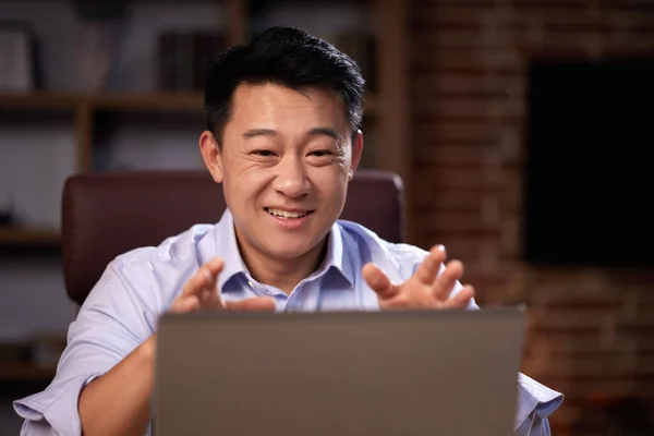 ラップトップのウェブカメラを使ってオンラインのウェビナーを開いているアジア人男性は 自宅のオフィスに座っている オンライン会議をして遠隔で通信している男コンピュータ画面を見て ストックフォト
