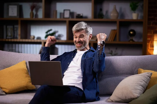 Hombre Emocionado Mirando Computadora Portátil Celebrando Éxito Mientras Sienta Sofá — Foto de Stock