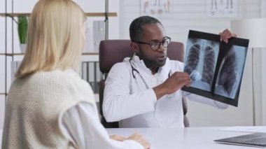 Afrikalı Amerikalı doktor, hasta kabul ediyor, şikayetleri dinliyor, tanı koyuyor. Akciğerlerin ve omurganın röntgenini gösteriyor. Doktor randevusu