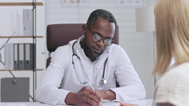 Medico Afroamericano Riceve Paziente Ascolta Lamentele Diagnosi Scrive Dati Nomina — Video Stock