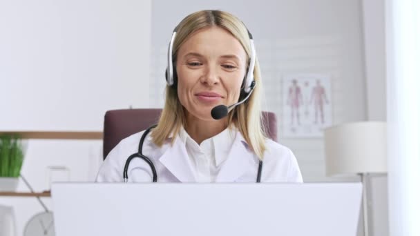 テレメディシンだ カメラを見てヘッドフォンで笑顔の女性医師のヘッドショットの肖像画 女性医師は 患者との仮想オンライン会議でリモートで相談します オンライン医学 — ストック動画