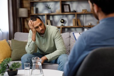 A visit to an African American psychologist. A man sits on a couch and talks to a psychotherapist. Depression, apathy, stress, burnout at work. Help of a psychologist clipart