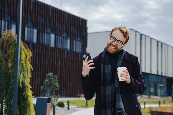 A young red-haired guy, a businessman in glasses, against the backdrop of an urban style, makes yes. Good luck in business, completed deal. Successful success