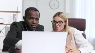 Ofisteki bir masada otururken iki kişi dizüstü bilgisayardaki belgeleri analiz ediyor. Ofisteki iş ortakları projeleri tartışıyor. Çok ırklı işbirliği.