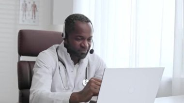 Afrikalı Amerikalı erkek doktor, online hasta danışmanlığını dizüstü bilgisayarında karşıladı. Teletıp hizmeti veren bir ofis. Online tıp ve teletıp kavramı