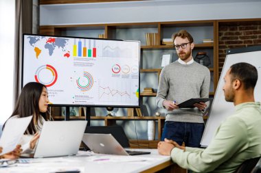 Takım lideri gülümseyen genç çokuluslu meslektaşlarına şirket geliştirme stratejisini açıklıyor. Mutlu çok ırklı iş adamları ofiste birlikte çalışmaktan hoşlanırlar. Başlangıç çalışması