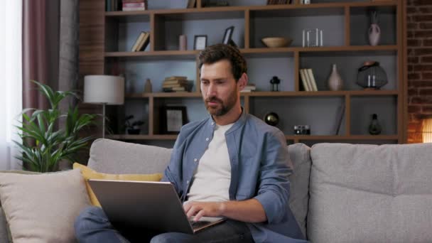 Przystojny Człowiek Pracujący Laptopie Siedząc Sofie Stylowym Mieszkaniu Wyluzuj Pracy — Wideo stockowe