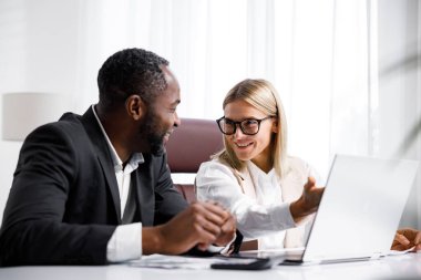 Ofisteki bir masada otururken iki kişi dizüstü bilgisayardaki belgeleri analiz ediyor. Ofisteki iş ortakları projeleri tartışıyor. Çok ırklı işbirliği.