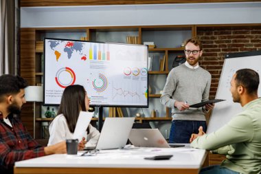 Takım lideri gülümseyen genç çokuluslu meslektaşlarına şirket geliştirme stratejisini açıklıyor. Mutlu çok ırklı iş adamları ofiste birlikte çalışmaktan hoşlanırlar. Başlangıç çalışması