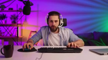 Gamer bearded guy, in a gaming headset, wins a video game. Cybersportsman in a neon room. Lifestyle gamer, online games. Victory in the E-Sport tournament.
