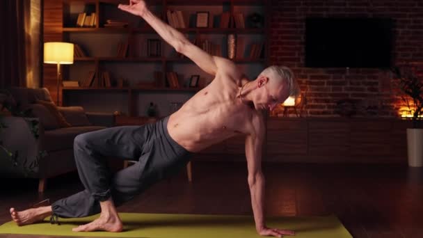 家でヨガ 白髪の男はアサナをやって 自宅でヨガをします スポーツ ストレッチ 高齢者の体操 古い時代の健康的なライフスタイル — ストック動画