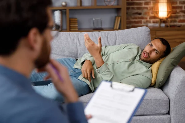 A visit to the psychologist of an African American man. A handsome man is lying on the couch and talking to a psychotherapist. Depression, apathy, stress, burnout at work. Help of a psychologist